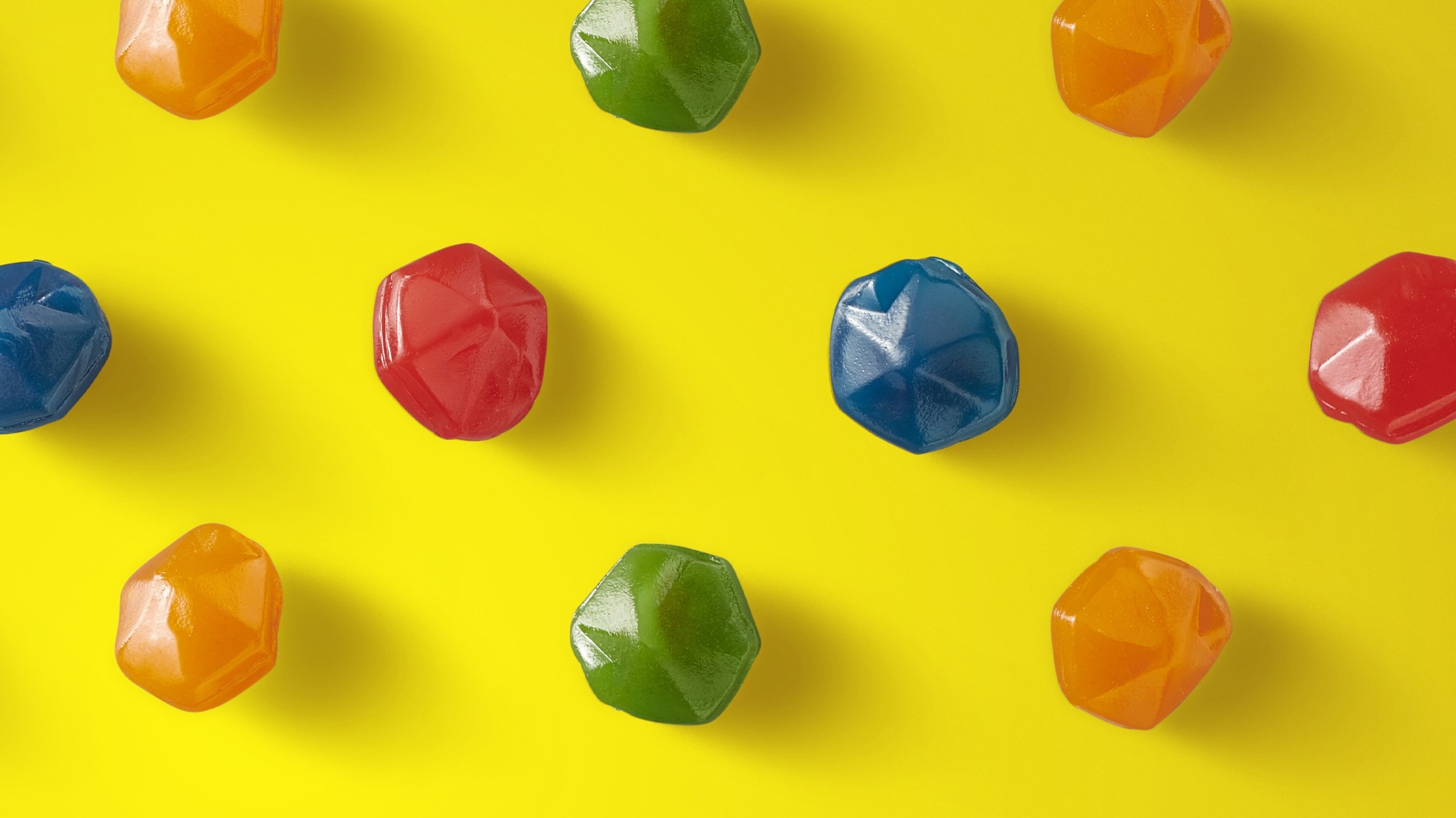 Colorful gem-shaped gummy candies arranged on a yellow background.