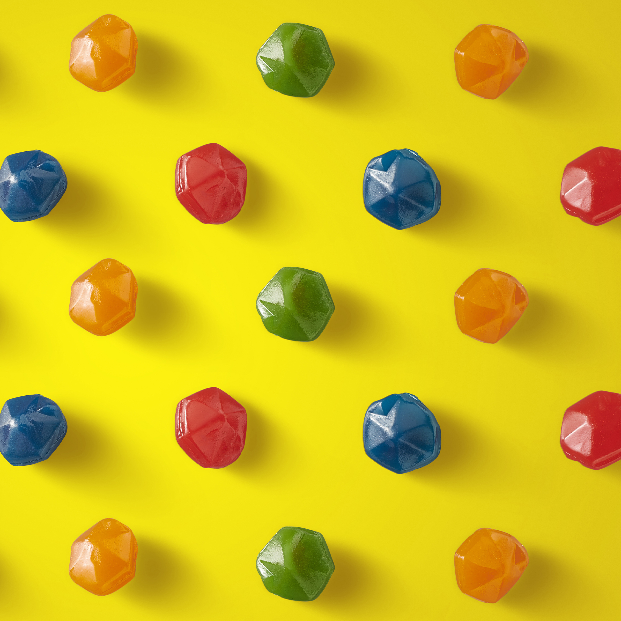 Colorful gem-shaped gummy candies arranged on a yellow background.